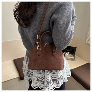 Detailed macro view of the brown suede shell bag with floral embossing and gold hardware