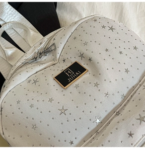 Detailed close-up of white leather backpack featuring silver star rivets and brand logo plate