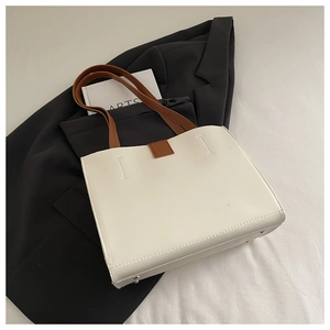Detail view of white leather tote bag featuring brown straps and protective metal feet