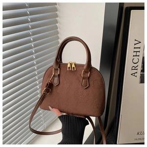 Close-up of brown shell bag showing embossed clover pattern and golden dual zippers