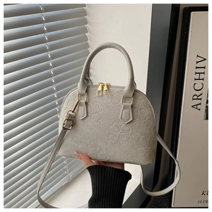 Close-up of embossed clover pattern on grey suede crossbody shell bag with gold zippers
