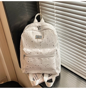 Detail of white backpack featuring silver star patterns and polished metallic brand logo