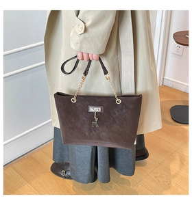 Detail view of brown suede tote bag with golden chain handle and small deer charm