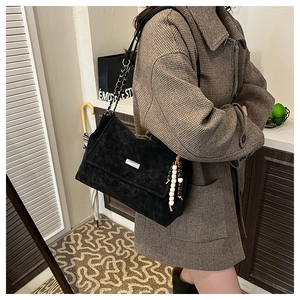 Détail du sac à bandoulière noir mat avec chaîne argentée et pompon en perles de bois