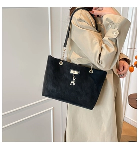 Close-up of black suede tote bag with gold deer pendant and elegant chain strap detail