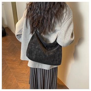 Détail macro d'un sac cabas vintage noir mat porté à l'épaule avec un manteau gris