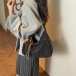 Sac croissant noir en similicuir suédé avec breloques sur un mannequin en manteau gris