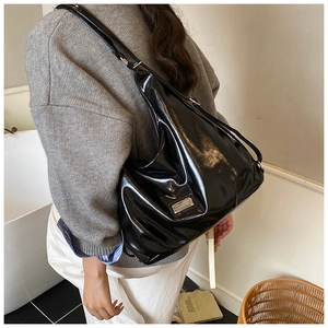 Close-up of a glossy black patent leather shoulder bag with sleek metallic logo detail