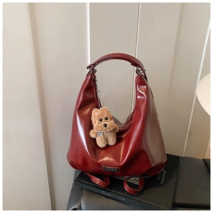 Detail of burgundy patent leather hobo bag with plush dog charm on a stack of books