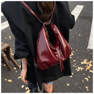 Detalle de un bolso tote burdeos brillante con borlas y detalles de la correa para hombro