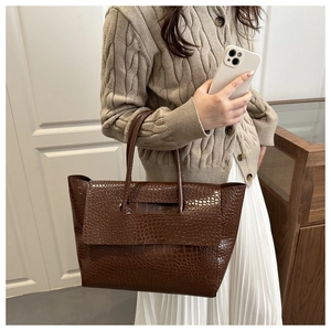 Detail of dark brown crocodile pattern tote bag held by model in elegant beige outfit