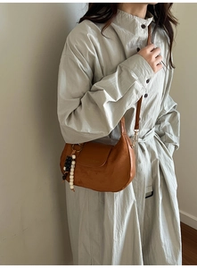 Detail of a brown crescent shoulder bag featuring wooden beads and smooth leather texture