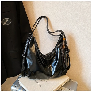 Detalle de bolso hobo de cuero brillante negro con correa y colgante trenzado