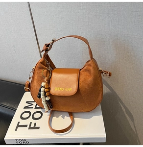 Brown suede crescent bag detail with wooden bead tassel and textured leather finish