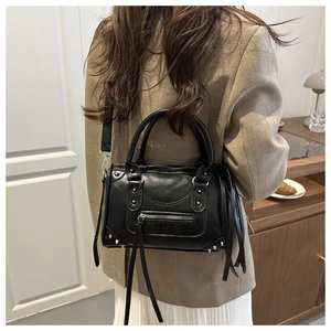 Model wearing a black Boston bag with silver rivets and long hanging leather tassels