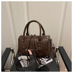 Detail of dark brown Boston bag featuring silver rivets and adjustable strap in studio