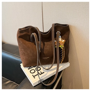 Detail of dark brown matte tote bag featuring contrast stitching and a cute bear charm