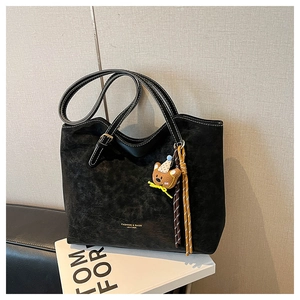 Detail of black tote bag with white stitching and decorative bear charm on a book