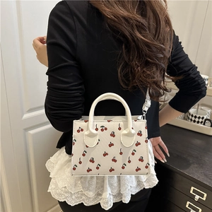 Mini white handbag with red cherry pattern, featuring handles and a shoulder strap