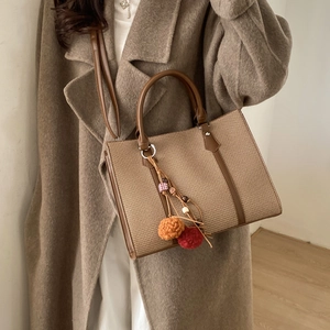 Minimalist woven tote bag with brown leather handles and pom-poms for daily commuting use