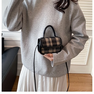 Detail of checkered wool handbag with black leather handle in minimalist indoor setting
