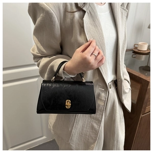 Classic black leather crossbody bag with gold twist lock worn with a beige blazer