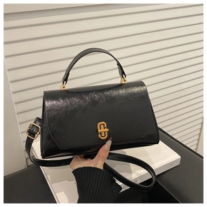 Close-up of black glossy textured leather handbag with a gold rectangle twist lock