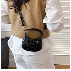 Detail view of mini black glossy crossbody bag with dual bow accents on a female model