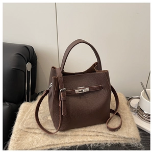Detail of dark brown lychee textured leather bucket bag with metal turn-lock on a soft rug