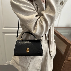 Fashionable black glossy leather handbag with gold buckle shown on a model