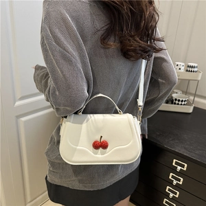 White faux leather crossbody bag with red cherry buckle shown on model in stylish home