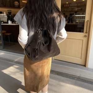 Sac hobo en daim marron foncé avec chaîne argentée et texte mode dans un décor de rue chaleureux