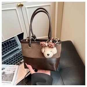 Dettaglio borsa a secchiello marrone con ciondolo peluche e texture in pelle mista