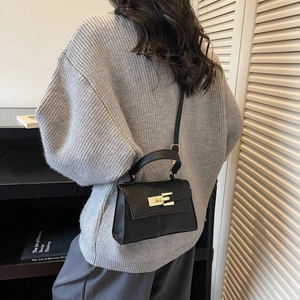 Classic black leather crossbody bag with golden buckle shown in a stylish indoor setting