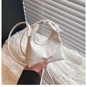 Detail view of white PU leather crescent bag with top handle and brand lettering
