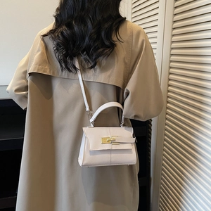 Beige minimalist crossbody bag with gold twist lock on a model in trench coat