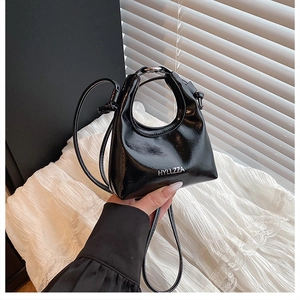 Detail of black patent leather handbag featuring silver logo and slim shoulder strap