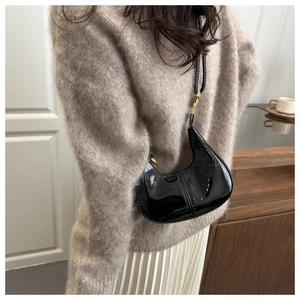 Sac croissant en cuir verni noir brillant porté à l'épaule dans un cadre de café élégant