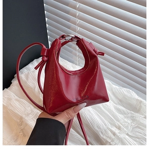 Close-up of wine red patent leather handbag featuring silver metal handle and embossed logo