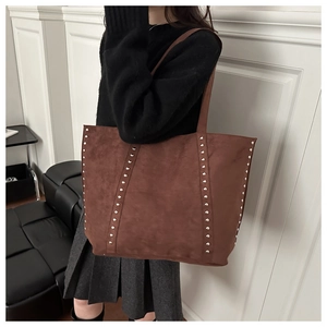 Détail du sac cabas en daim marron avec clous argentés porté par le mannequin