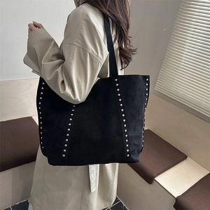 Grand sac cabas en daim noir avec rivets vintage porté à l'épaule dans un décor épuré