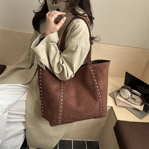 Grand sac cabas en daim marron avec rivets porté par un mannequin en trench-coat