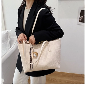 Close-up of minimalist off-white crocodile texture tote bag with baseball pendant detail