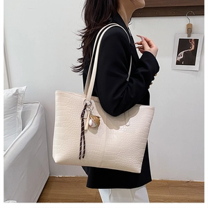 Model showing cream crocodile pattern tote bag with baseball pendant in modern room