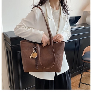 Close-up of brown crocodile pattern tote bag with plush charm on a woman in white blazer
