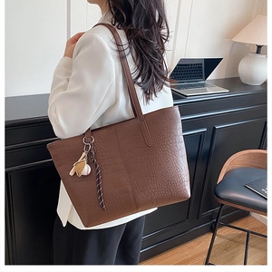 Brown crocodile texture tote bag with sports charms shown in a modern office setting
