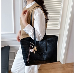 Detail of black tote bag with crocodile pattern and baseball charms on a model