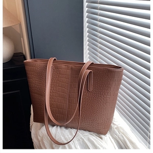Detail of caramel tote bag showing crocodile pattern texture and long shoulder straps