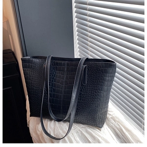 Close-up of black crocodile-embossed leather texture on a stylish tote bag with long straps
