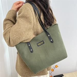 Dark green corduroy tote bag with black leather straps shown on a model's shoulder